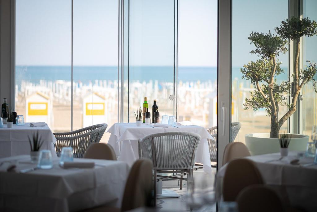 a restaurant with white tables and chairs and windows at Unico Hotel Caorle in Caorle