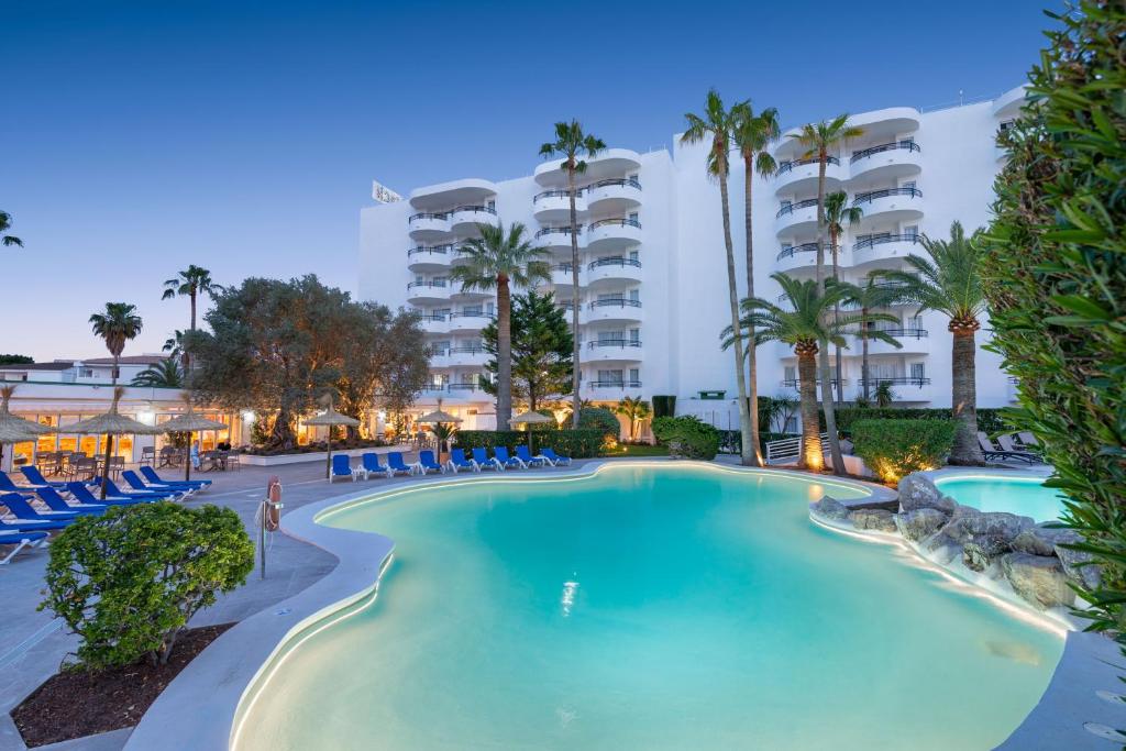 a pool at a resort with palm trees and chairs at Alcudia Beach Apartments in Port d'Alcudia