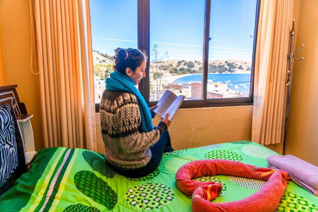 una mujer sentada en una cama leyendo un libro en SKYLAKE B&B, en Copacabana