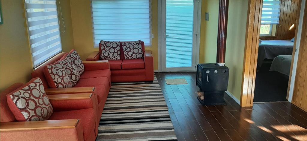 a living room with two red couches and a wood stove at Cabañas Quimantu-Aguas Calientes in Puerto Varas