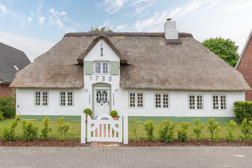una casa blanca con techo de paja con una puerta en De ole Hüs 1735, en Braderup