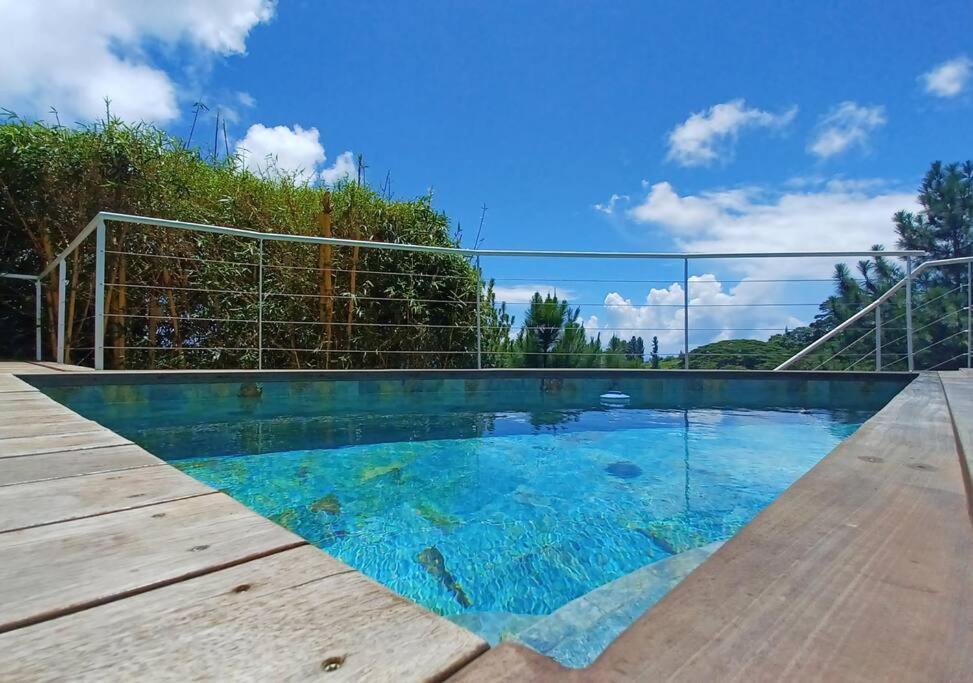 a swimming pool with blue water and a wooden deck at Logement Cosy avec Piscine et Vue Tahiti Punaauia in Punaauia
