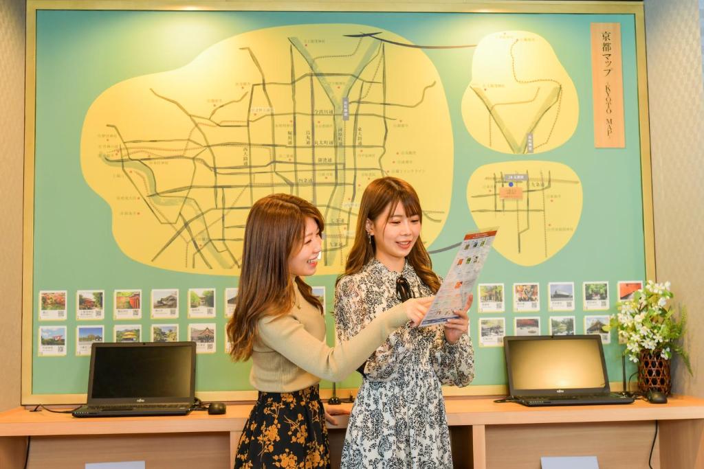Duas mulheres numa sala a segurar um pedaço de papel. em Sanco Inn Kyoto Hachijoguchi Shikinoyu em Quioto