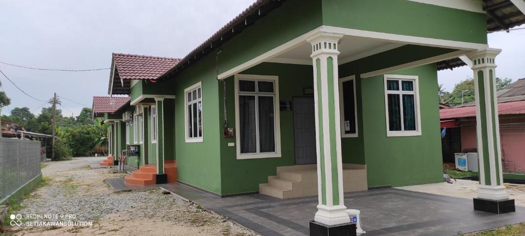 a green house with white columns on a street at Homestay Anjung Ismail Anjung Rahmah in Kampong Pauh