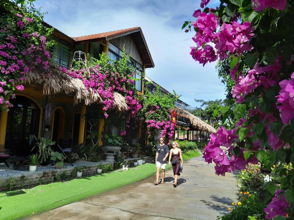 two people walking down a path in front of a building with flowers at Amazing View Homestay in Ninh Binh