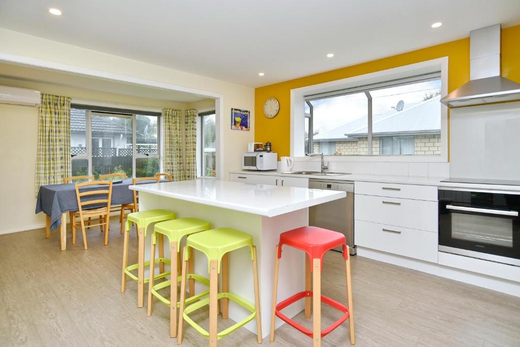 une cuisine avec des tabourets colorés autour d'un comptoir blanc dans l'établissement Charlesworth Villa - Christchurch Holiday Homes, à Christchurch