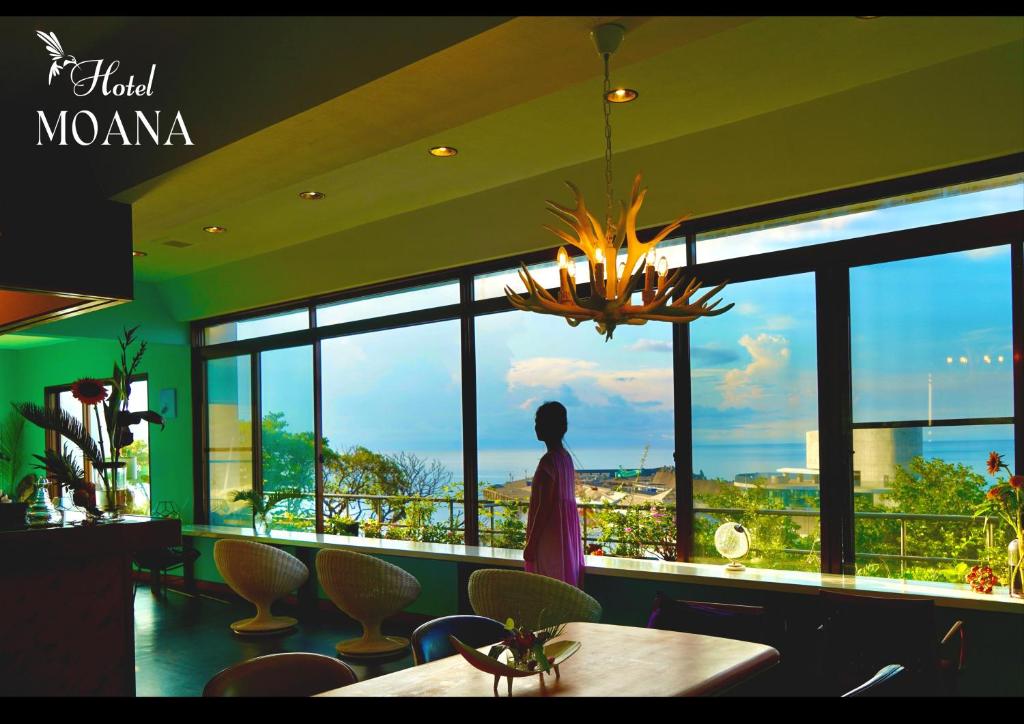 una mujer parada frente a una habitación con una gran ventana en Hotel MOANA絶景オーシャンビューカフェラウンジ en Oshima