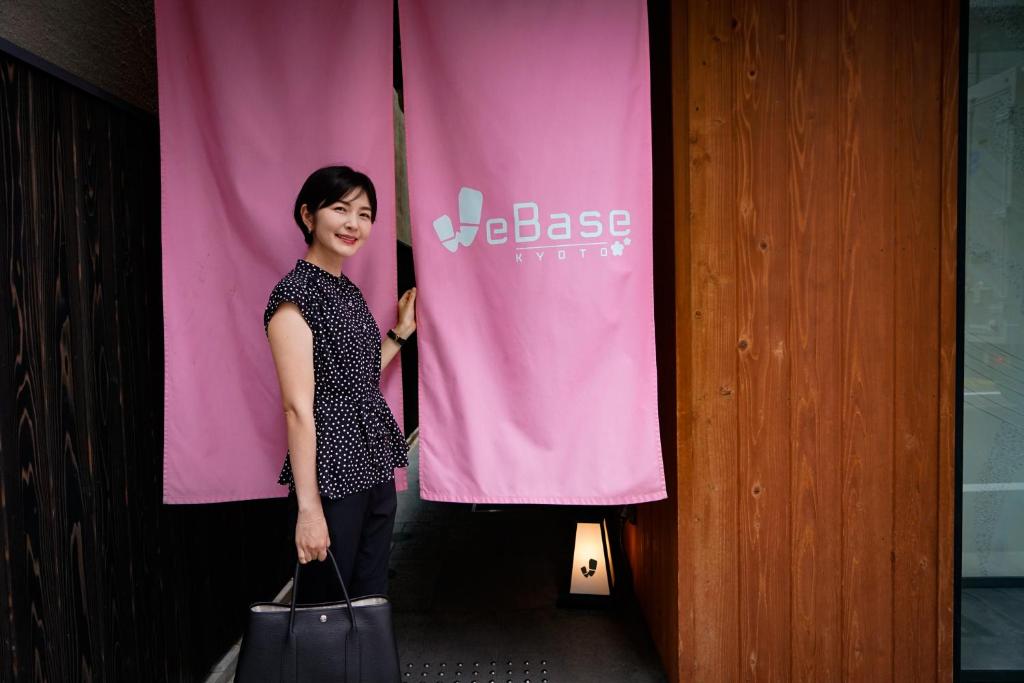 a woman standing in front of a pink banner at WeBase Kyoto in Kyoto