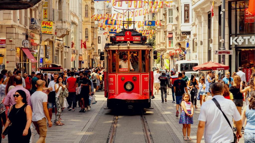 a red trolley car driving down a busy city street at Taksim Leon's Hotel in Istanbul