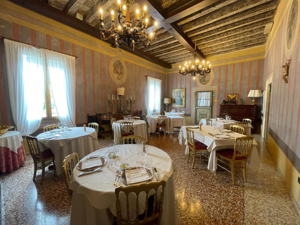un restaurant avec des tables et des chaises blanches et un lustre dans l'établissement Hotel AB Baretta, à Legnaro