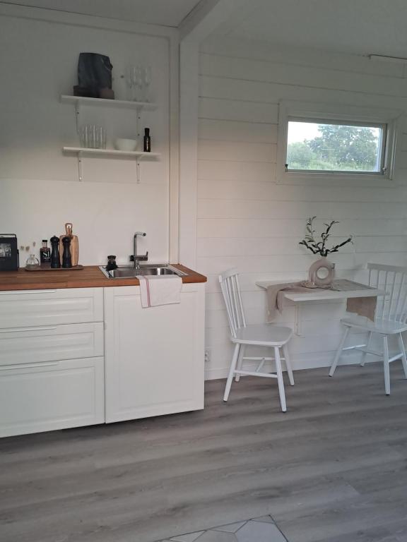 a kitchen with white cabinets and a sink and chairs at Attefallshuset in Hyllinge