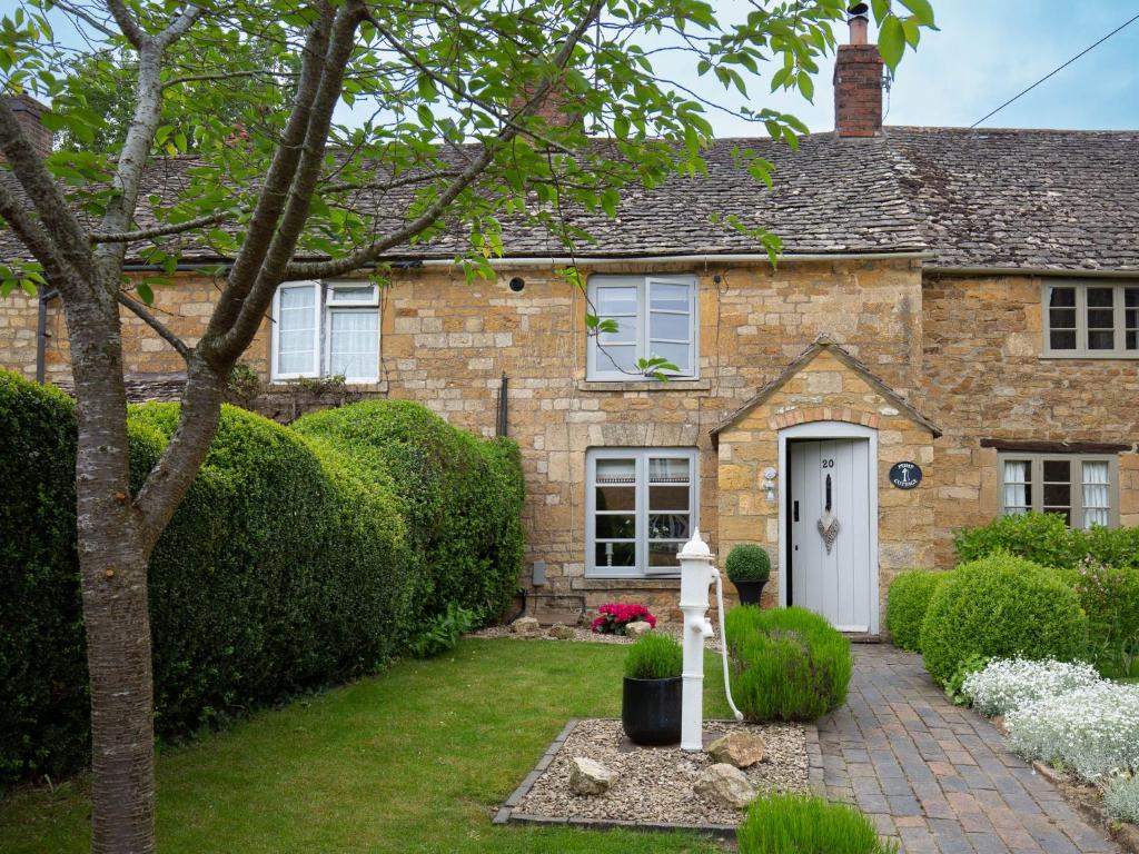 una casa de ladrillo con una puerta blanca y un patio en High Pump Cottage, en Chipping Campden