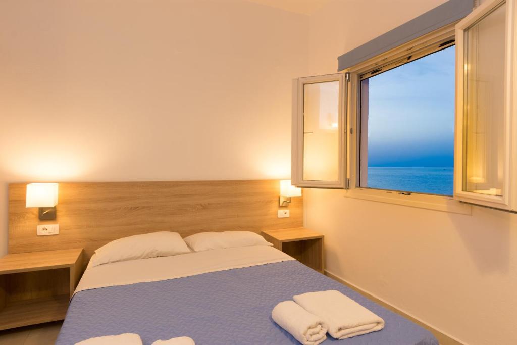 a bedroom with a bed and a window with the ocean at Socrates Apartmens & Restaurant in Milatos