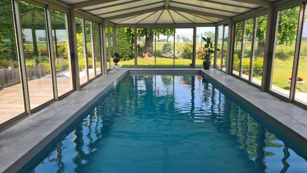 uma piscina interior com um jardim de Inverno com janelas em Villa 5*, mer à 3 mn, piscine intérieure à 28° em Gonneville-en-Auge