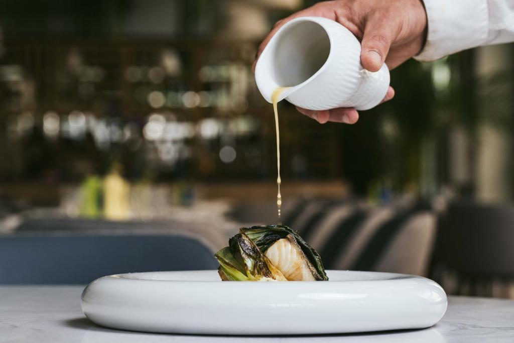 a person pouring sauce onto a plate of food at Martinhal Lisbon Oriente in Lisbon