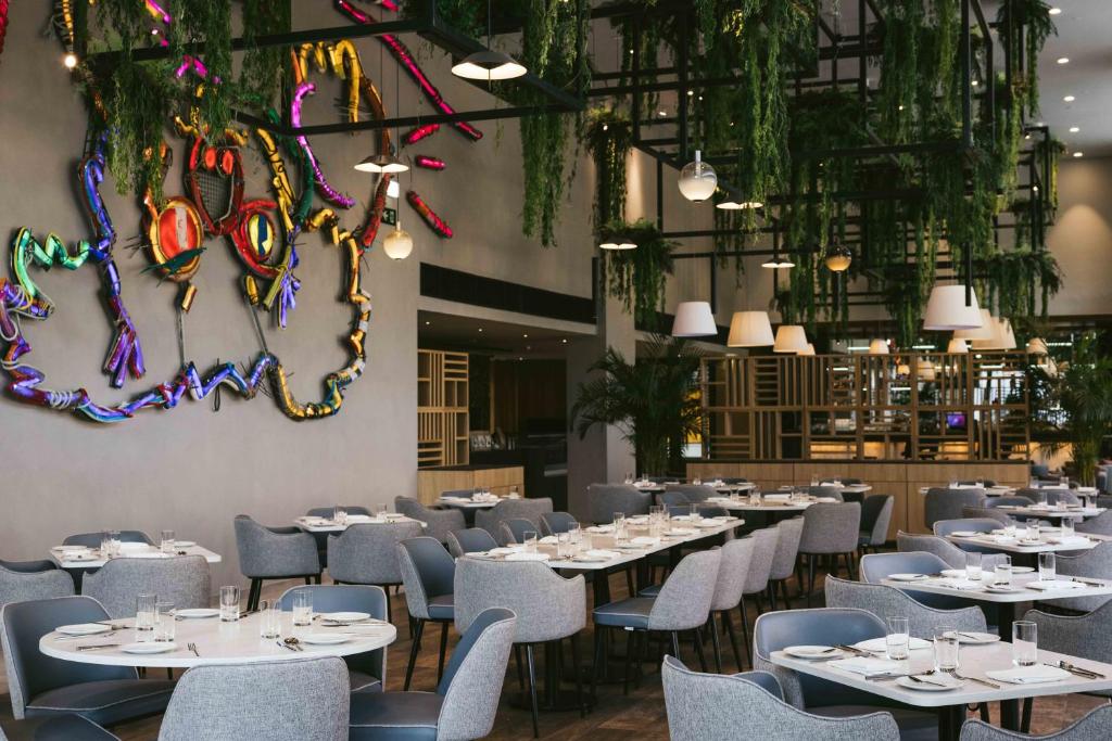 a restaurant with white tables and chairs and plants at Martinhal Lisbon Oriente in Lisbon