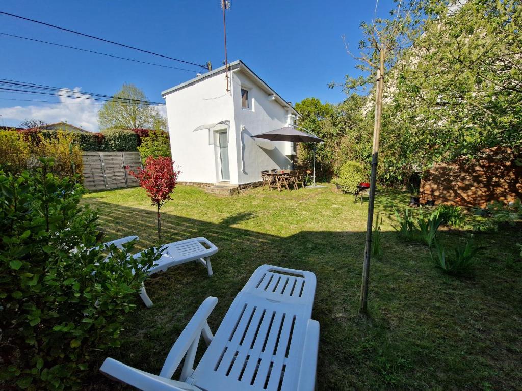 zwei weiße Bänke in einem Hof mit einem weißen Haus in der Unterkunft Tiny house avec jardin spacieux in Saint-Nazaire