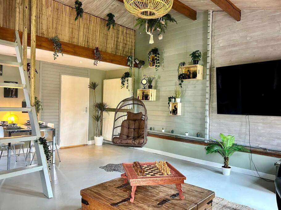 uma sala de estar com uma mesa e uma televisão em Jungle style lodge with jacuzzi ,sauna and garden near Amsterdam em Vijfhuizen