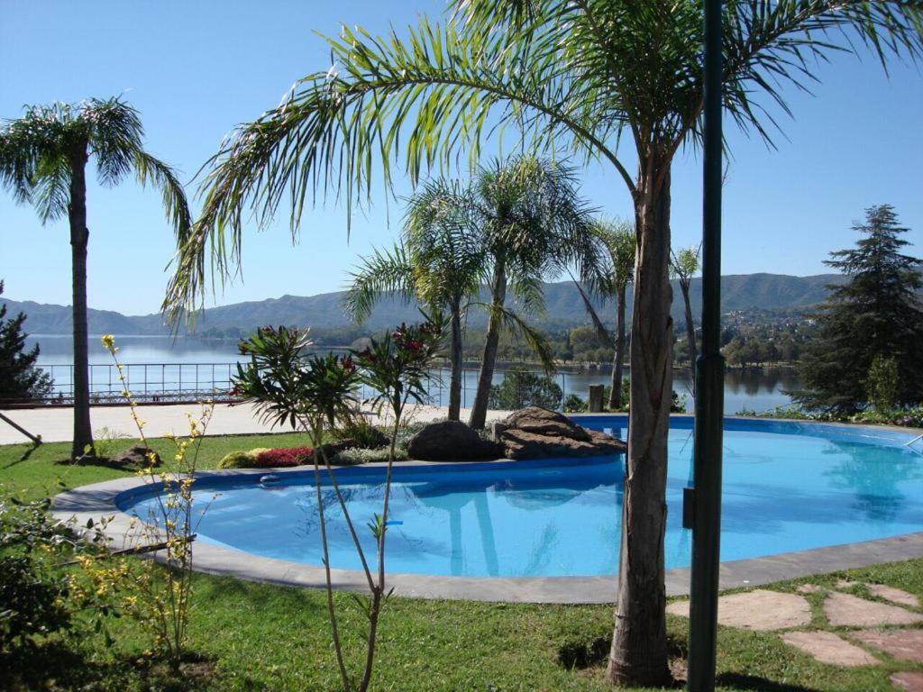 a swimming pool with palm trees next to a lake at casa con vista y bajada al lago in Villa Carlos Paz