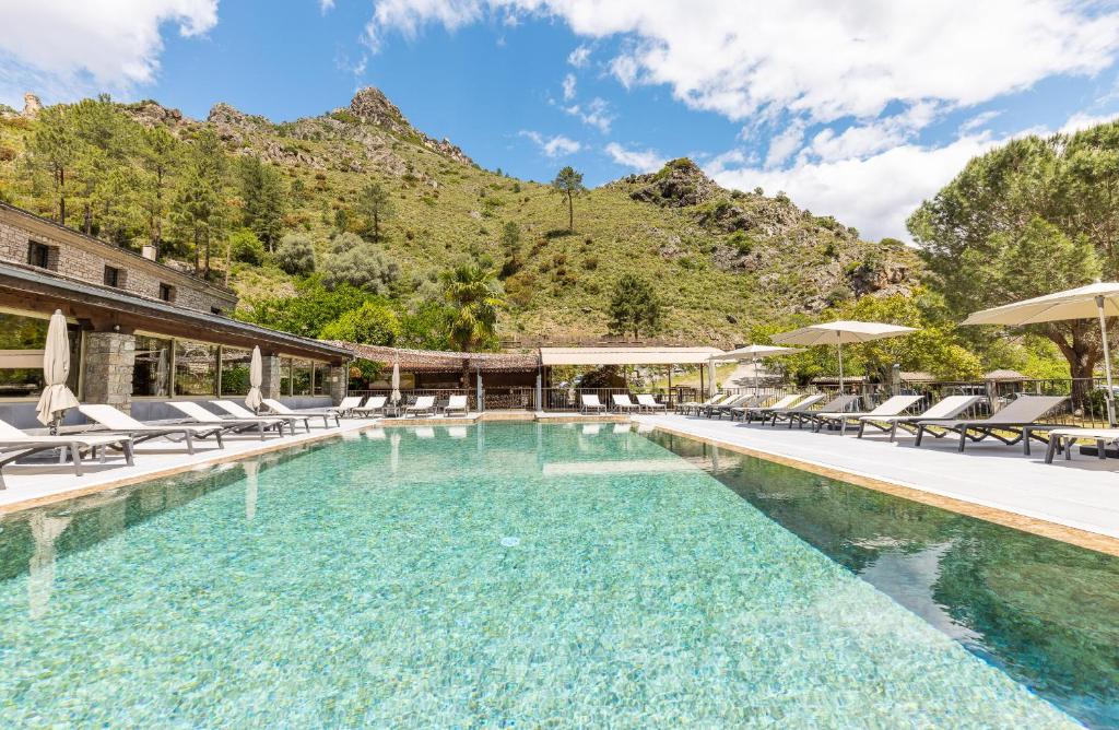 una piscina con sillas y una montaña en Hôtel de la Restonica en Corte