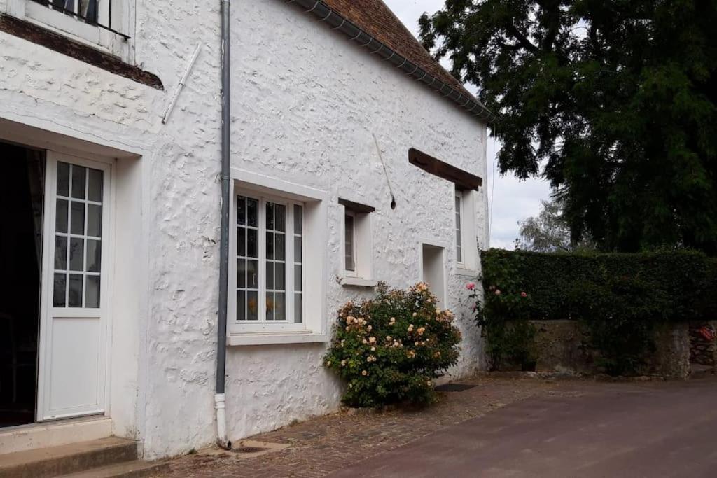 un bâtiment blanc avec une fenêtre et un buisson de fleurs dans l'établissement Bel appartement dans un magnifique domaine du XVIe, à Autouillet