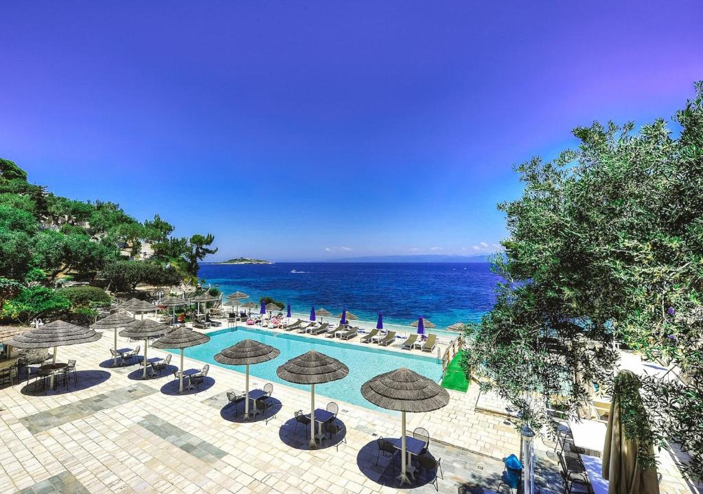 a pool with umbrellas and chairs and the ocean at Agali Hotel Paxos in Gaios