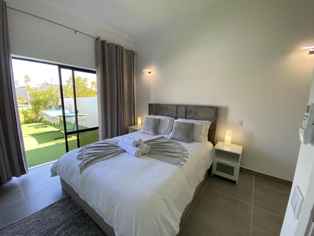a bedroom with a white bed with a large window at Casa com terraço e piscina Sagres in Sagres