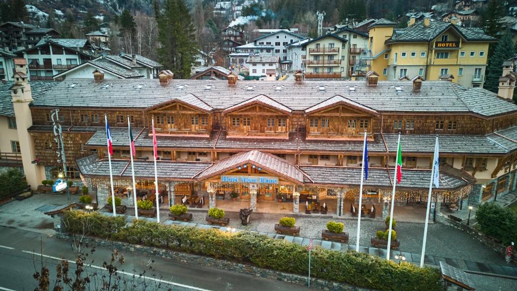 een groot houten gebouw met vlaggen ervoor bij iH Hotels Courmayeur Mont Blanc in Courmayeur
