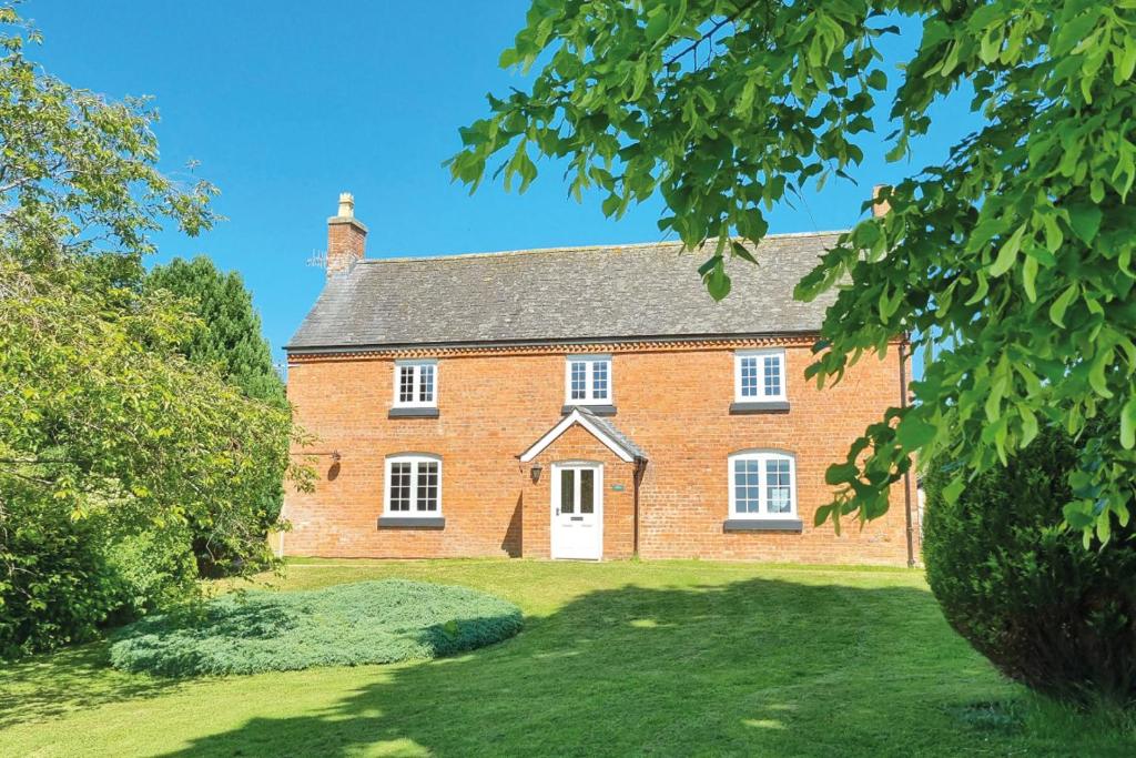 a large red brick house on a green lawn at Calcot Farmhouse in Chirbury