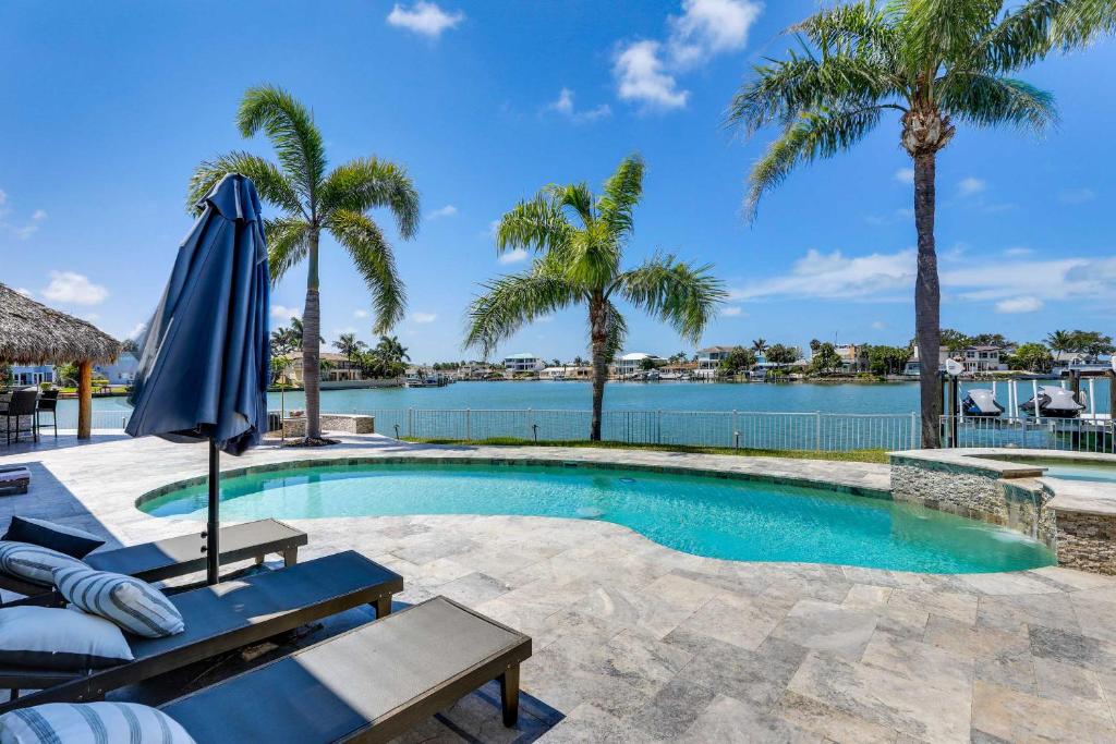 a swimming pool with a blue umbrella and palm trees at Luxury St Petersburg Home with Pool and Bay Access! in St Pete Beach