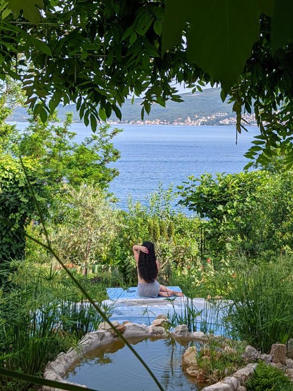 a person sitting on a rock in the water at Apartmani VERONA in Bijela