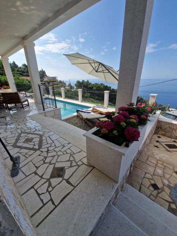 un patio con flores y una sombrilla junto a una piscina en Amazing sea view place with swimming pool, en Sveta Nedelja