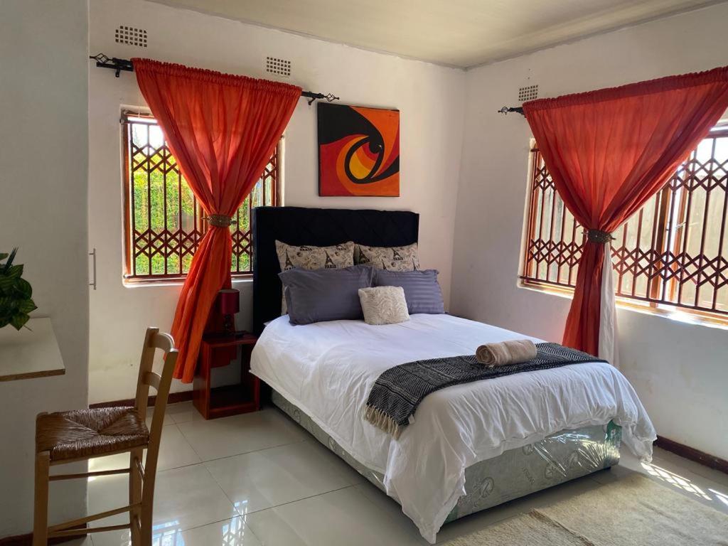 a bedroom with a bed with red curtains and a chair at Samkab Legacy & comfort Ndeke (airport) in Lusaka