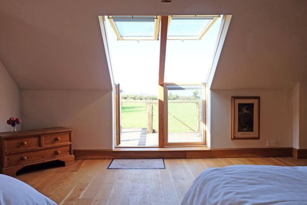 um quarto com uma cama e uma grande janela em A stunning converted barn offering country life. em Chewton Mendip
