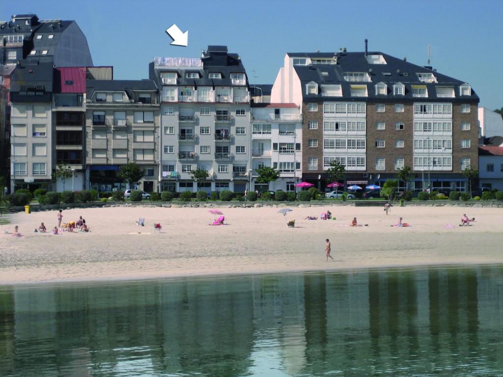 un groupe de personnes sur une plage avec un bâtiment dans l'établissement Duerming Portonovo Picó, à Portonovo