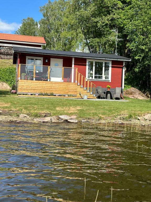 una casa roja con una terraza junto a un cuerpo de agua en Sommarstuga med sjötomt och brygga, en Hedemora