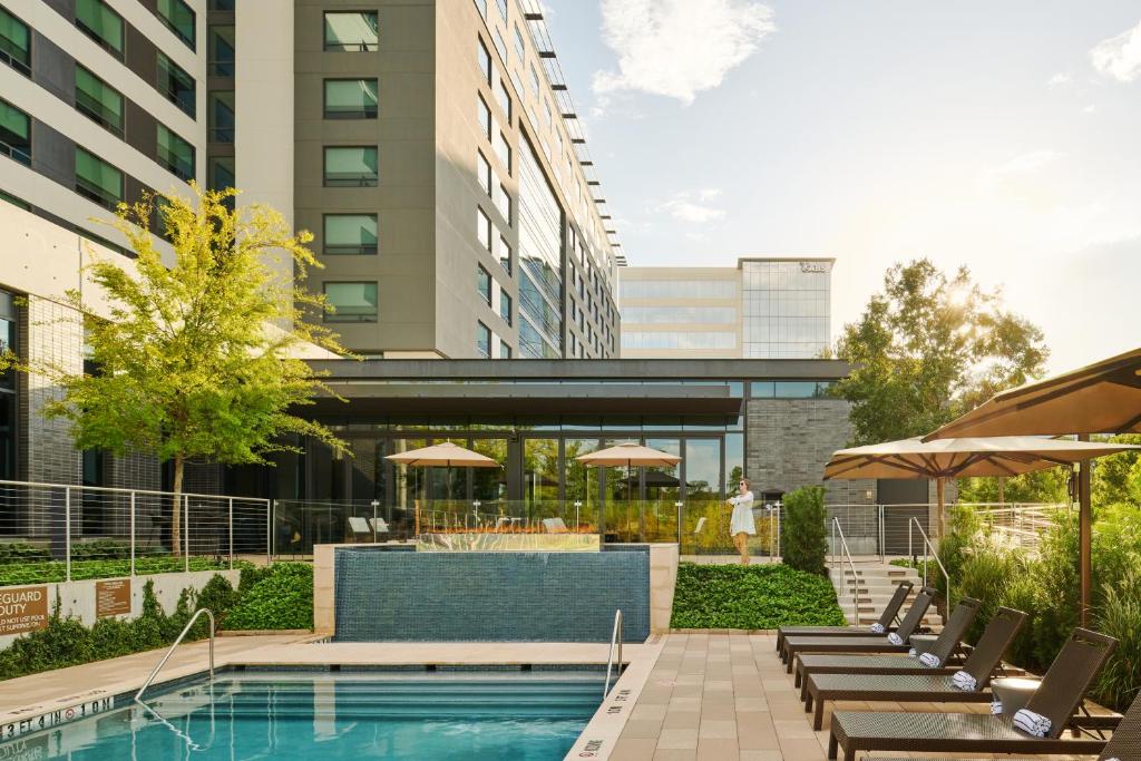 a pool with chairs and umbrellas next to a building at Houston CityPlace Marriott at Springwoods Village in The Woodlands