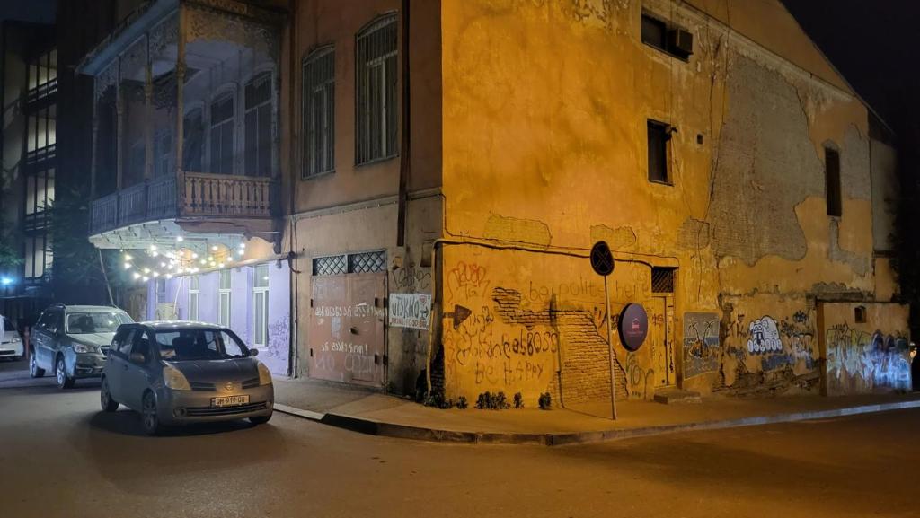 um carro estacionado ao lado de um edifício amarelo à noite em Orbeliani Hostel em Tbilisi