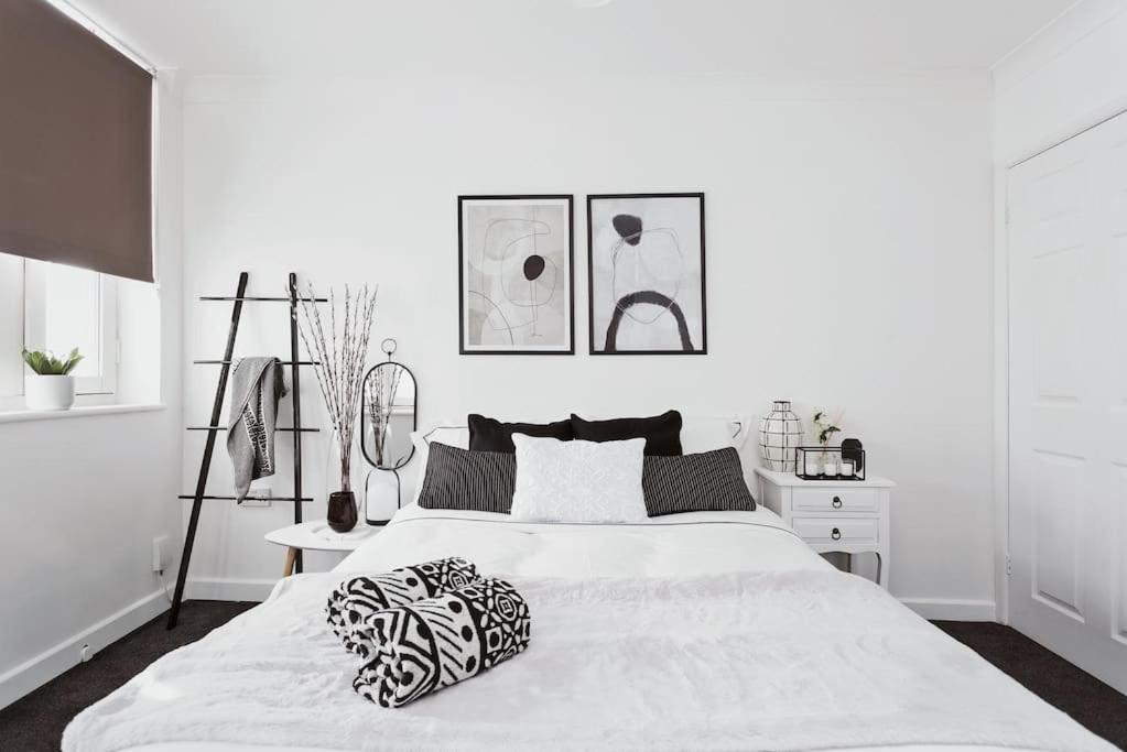 a white bedroom with a large white bed with black and white pillows at The Minimalist - Entire 1 bed flat near Gunwharf Quays, Ground Floor Flat Private Entrance in Portsmouth