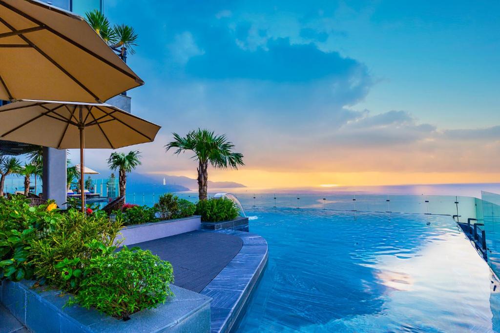 uma piscina com um guarda-sol e o oceano em Peninsula Hotel Danang em Da Nang