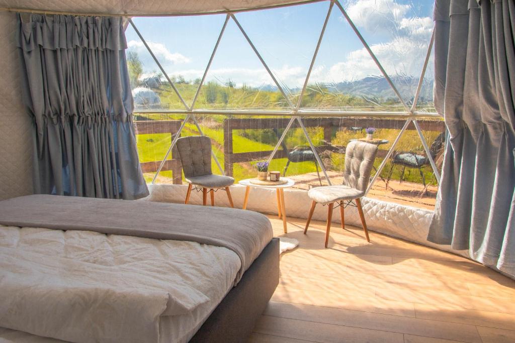 a bedroom with a bed and two chairs and a large window at Sanctum Glamping 