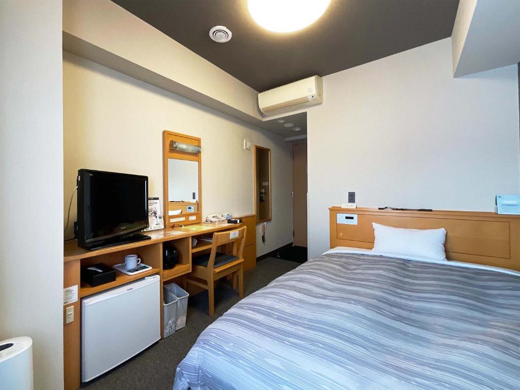um quarto com uma cama e uma secretária com uma televisão em Hotel Route-Inn Aizuwakamatsu em Aizuwakamatsu