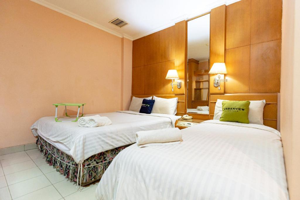 a hotel room with two beds and a mirror at Urbanview Hotel P Residence Asemka in Jakarta