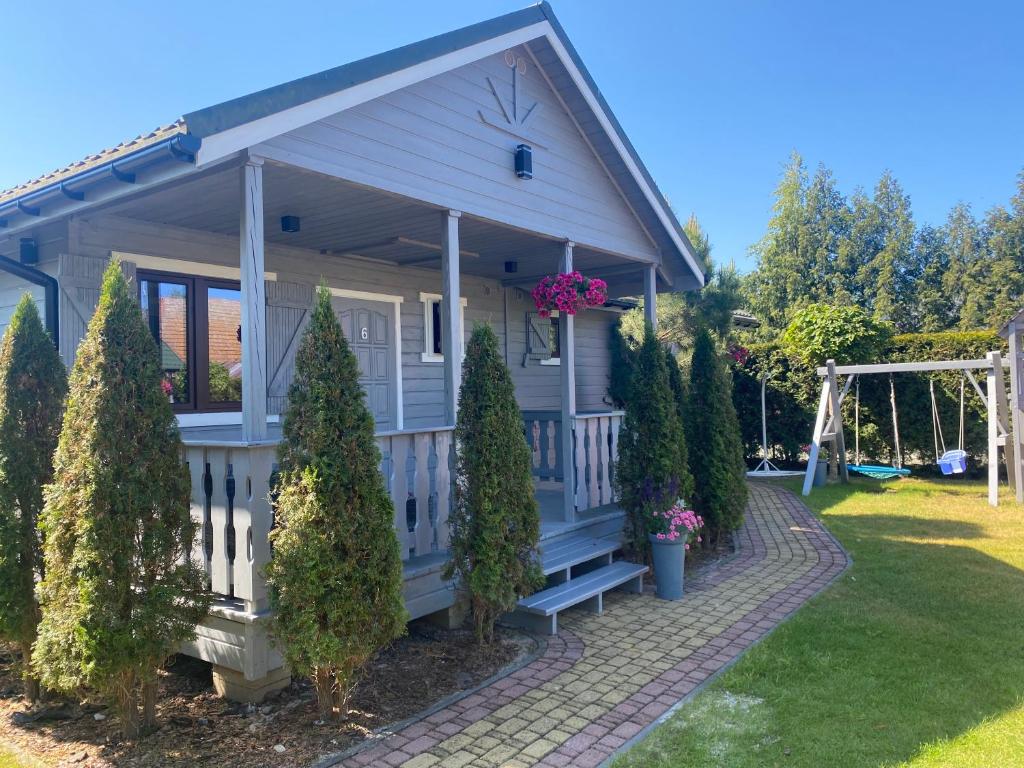 a small white house with a porch and some trees at Domki Letniskowe Bursztynek in Dąbki