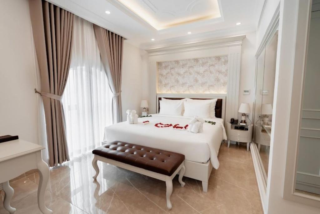 a white bedroom with a large white bed and a bench at MerPerle Beach Hotel in Nha Trang