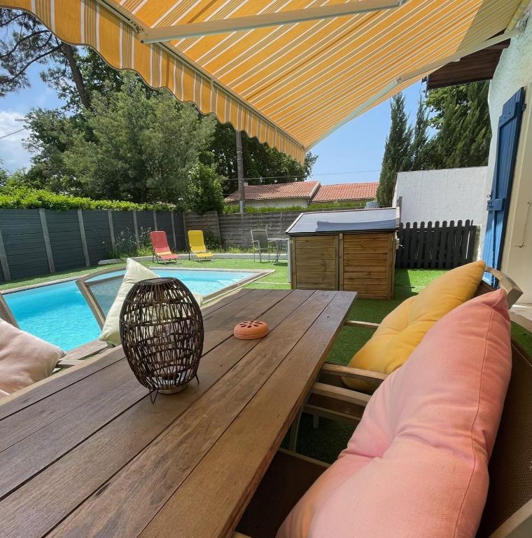une table et des chaises en bois sur une terrasse avec une piscine dans l'établissement Détente Piscine et jacuzzi au Bassin d'Arcachon, à Andernos-les-Bains