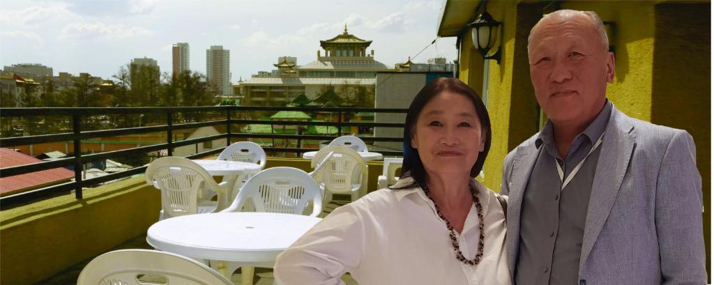 a man and woman standing on a balcony with tables and chairs at Gandan Terrace Guesthouse in Ulaanbaatar