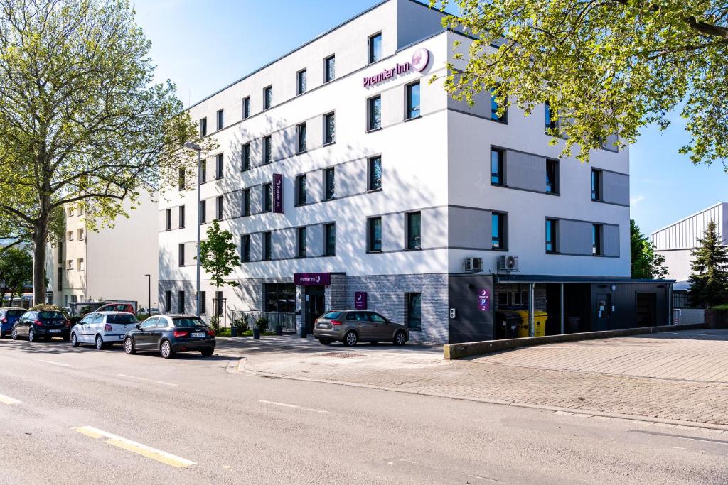 Premier Inn Heidelberg City Bahnstadt في هايدلبرغ: مبنى أبيض فيه سيارات تقف في موقف للسيارات