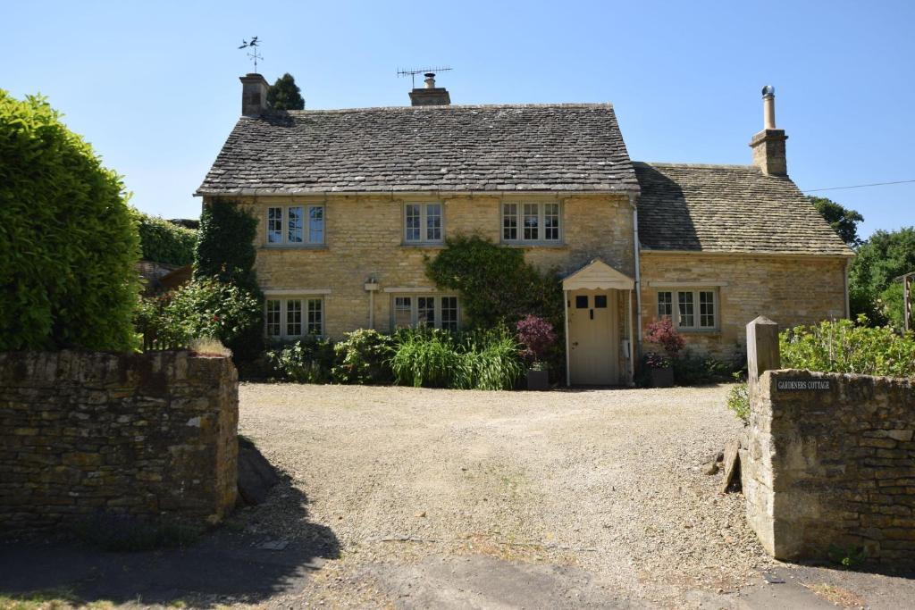 an old stone house with a gravel driveway at Gardeners Cottage in Shipton under Wychwood