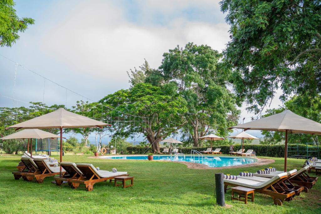 eine Gruppe von Stühlen und Sonnenschirmen neben einem Pool in der Unterkunft Taita Hills Safari Resort & Spa in Tsavo
